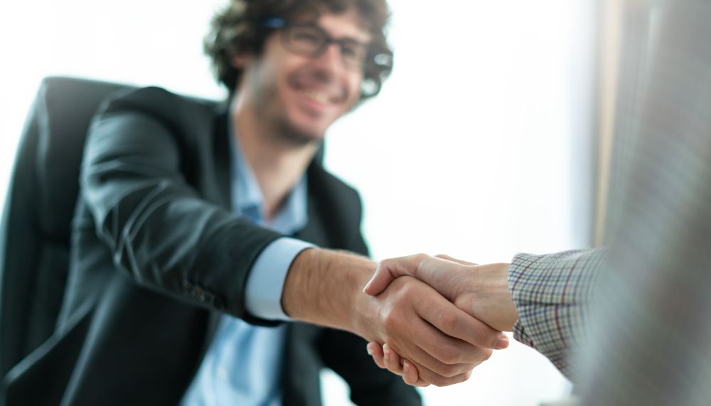A young man wearing glasses is shaking hands with someone who is not visible in the picture.