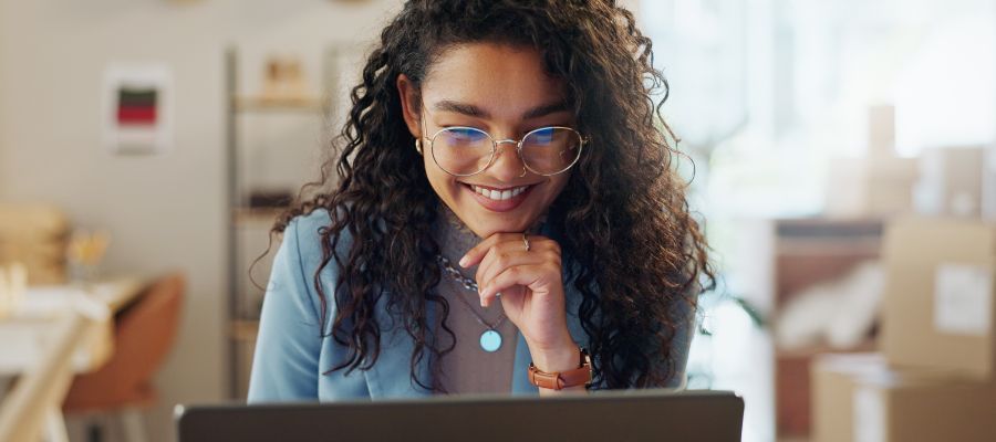 Une femme regarde un ordinateur portable en souriant.
