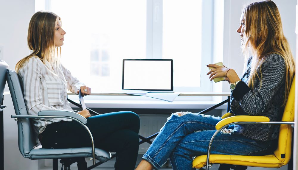 Profilansicht zweier junger Frauen in einer Interviewsituation vor einem Schreibtisch.