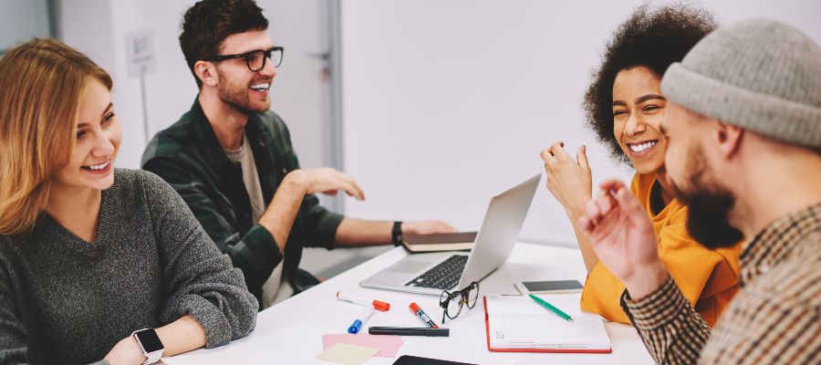 Quatre jeunes sont assis à un bureau devant un ordinateur portable et discutent.